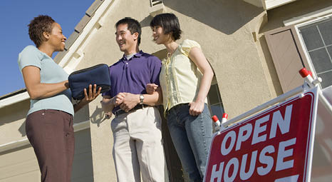 A couple speaking to a real estate agent in front of a home with an open house sign