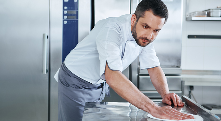 a man sanitizing a work surface in a kitchen