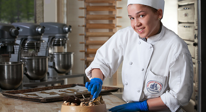 a women in a chef uniform cutting a beautifully decorated cake