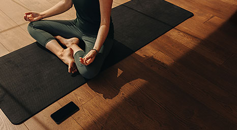 Person sits cross-legged on an exercise mat while meditating, with a smartphone nearby.
