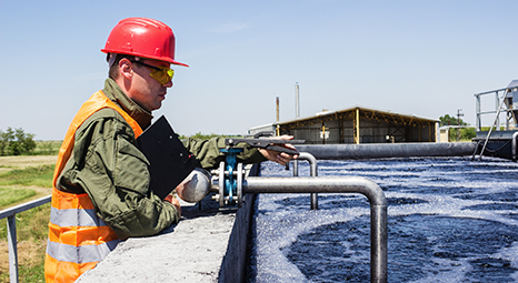 a man with a clipboard and hard hat looking out onto a water resevoir