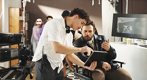 Film production crew members review footage together on a tablet while working on set.